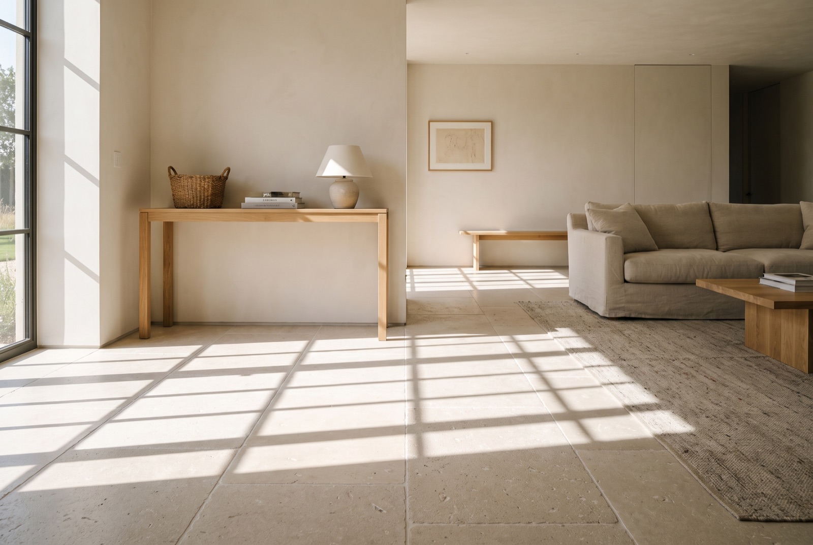 Honed French limestone floor in large-format slabs running from an entry hall through to a living room, with plaster walls and a white oak console