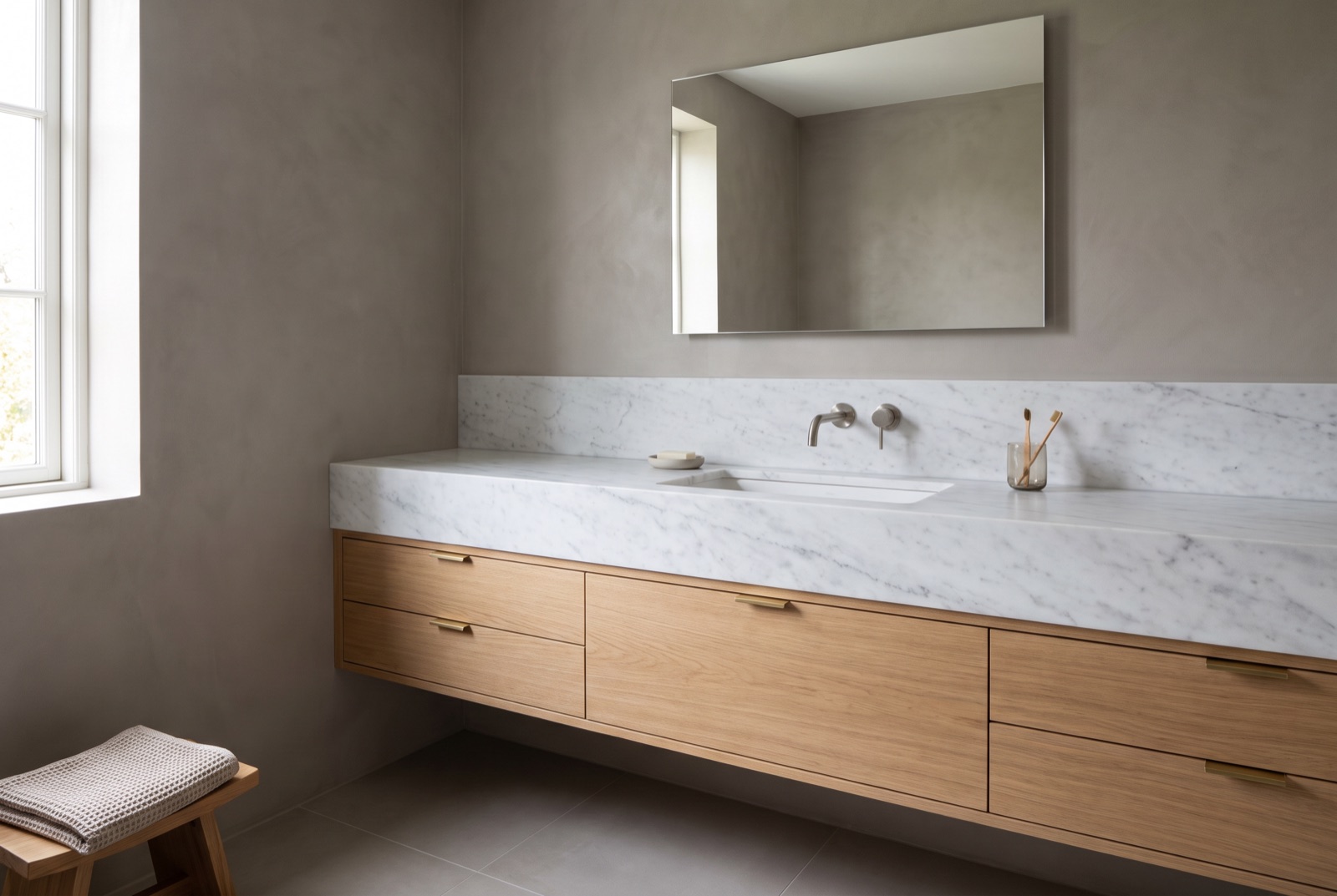 Honed Carrara marble vanity top with an integrated basin and a low integral backsplash, on a wall-mounted white oak cabinet against a microcement wall