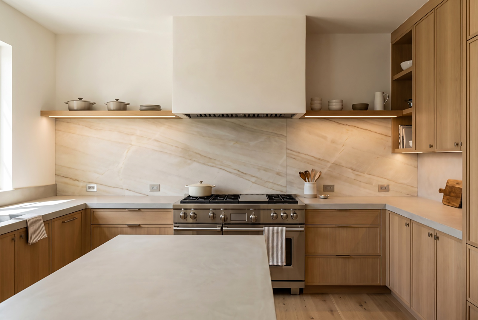 Quartzite full-height backsplash behind a professional range, running from the countertop to the underside of a plaster hood, with outlets set into quiet areas of the slab